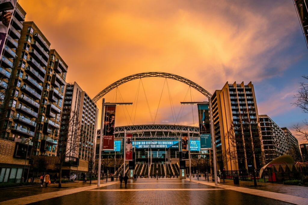 Olympic Way leading to Wembley Stadium and its arch under an orange sunset sky, with flats on both sides.