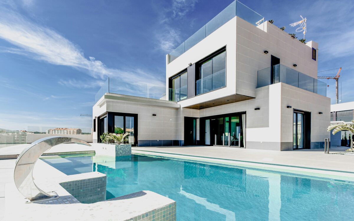 A white villa with a turquoise swimming pool